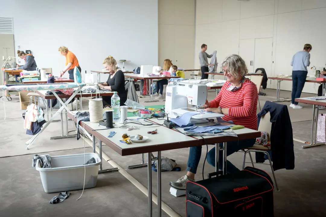 Teilnehmerinnen und Teilnehmer arbeiten bei der Nähaktion an verschiedenen Nähmaschinen