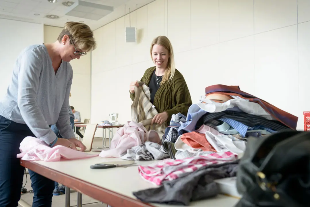 Teilnehmerinnen einer Nähaktion sortieren Stoff und Kleidung