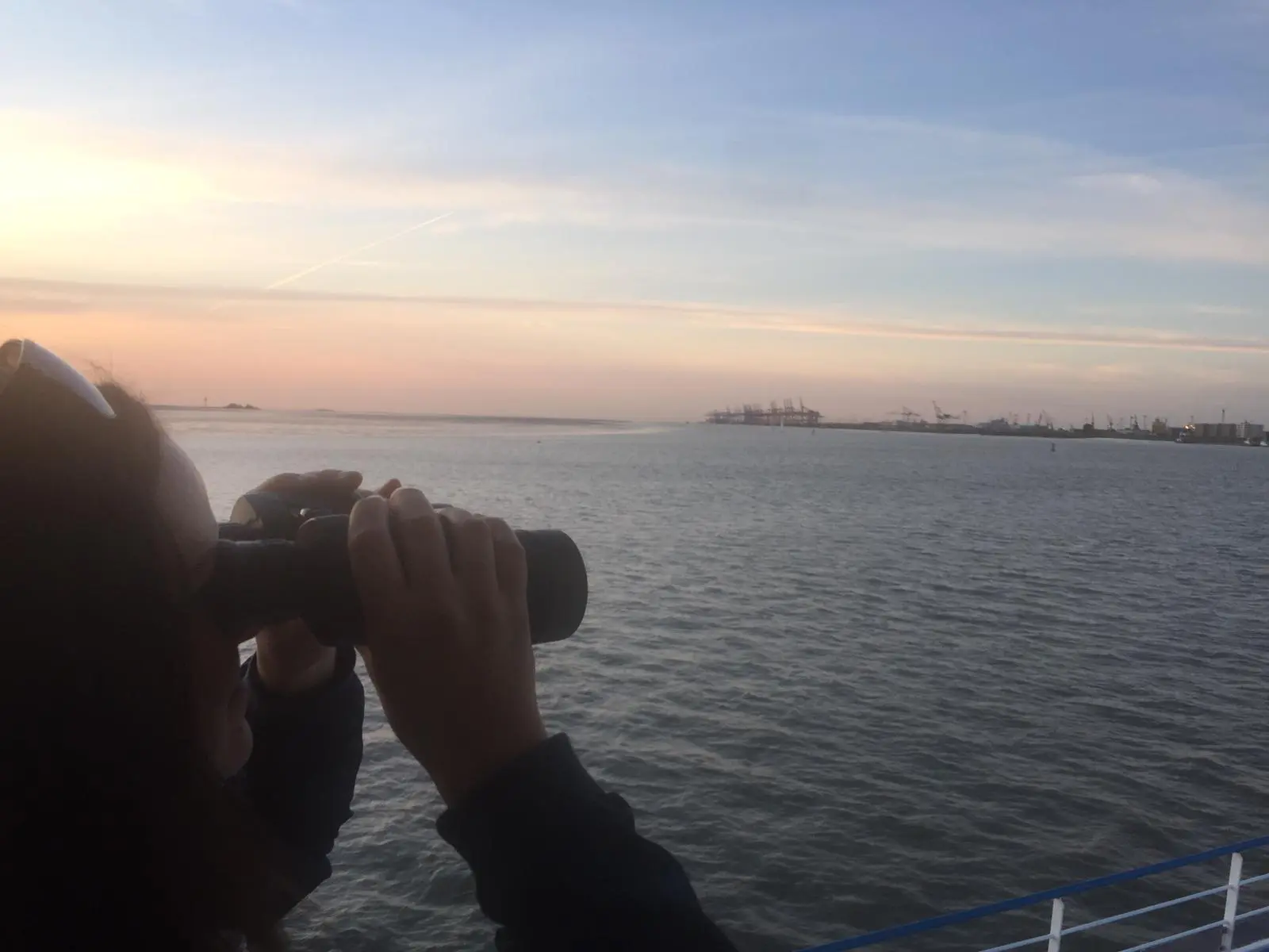 Lisa Keller hält ein Fernglas und blick auf über Wasser auf den Hafen