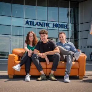 Eine Frau und zwei Männer sitzen auf einer Ledercouch im Freien vor dem Eingang des Atlantic Hotel Sail City