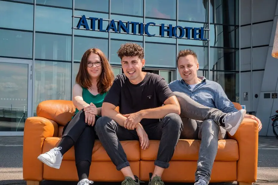 Eine Frau und zwei Männer sitzen auf einer Ledercouch im Freien vor dem Eingang des Atlantic Hotel Sail City