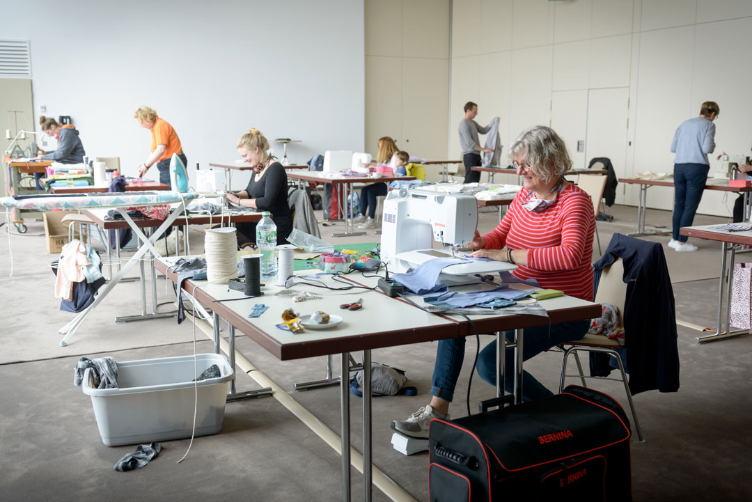 Teilnehmerinnen und Teilnehmer arbeiten bei der Nähaktion an verschiedenen Nähmaschinen