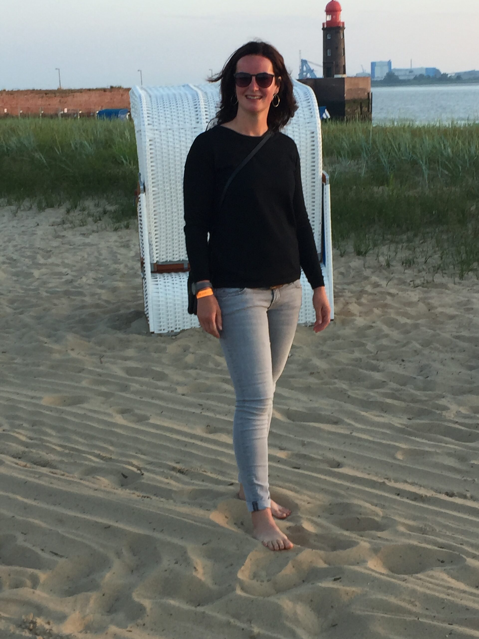Lisa Keller spaziert barfuß im Sand des Weserstrands vor einem weißen Strandkorb