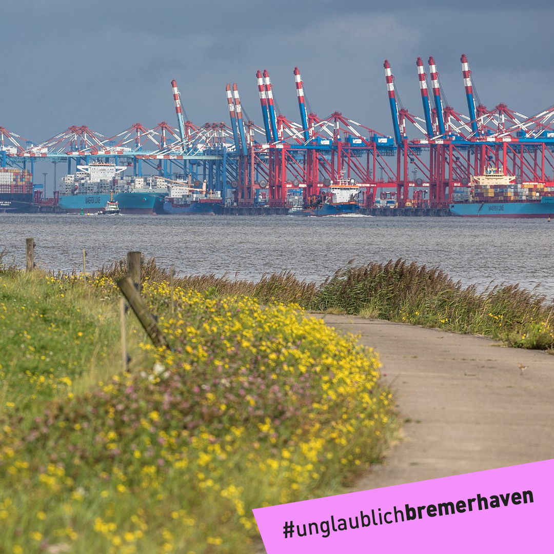 Text "#unglaublich bremerhaven" vor einem Wanderweg mit Grün am Wegesrand. Im nahen Hintergrund ist das Containerterminal zu sehen.